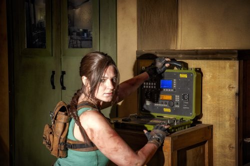 Lara Croft kneels before a radio case in front of a tent, looking back at the camera.